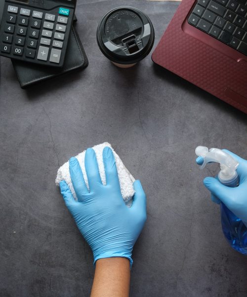 hand in blue rubber gloves holding spray bottle cleaning office table